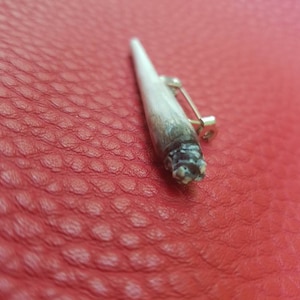 May include: A white and black pin shaped like a small, thin, wooden stick with a silver pin on the back.