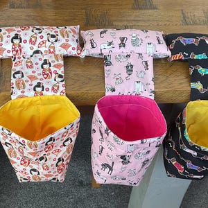 May include: A selection of fabric car tidy bags in different patterns. Each bag has a T-shaped top with patterned fabric and a contrasting interior. Patterns include floral, Japanese dolls, cats, dachshunds, and pink spots.