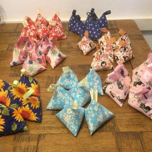 May include: A collection of 18 triangular fabric pouches with various patterns. The pouches are filled with dried herbs and flowers. The patterns include sunflowers, cats, and floral designs.