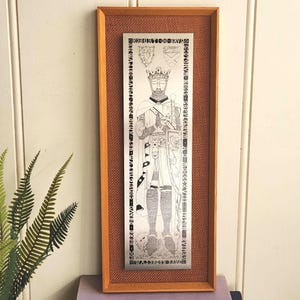 May include: A framed metal artwork featuring a detailed engraving of a crowned figure in armor, holding a sword and shield. The artwork is set against a textured brown background within a wooden frame. The text "ROBERT DE BRVS" is visible at the top.
