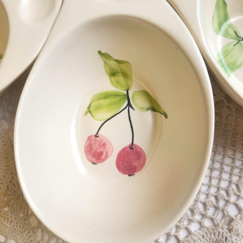 May include: Off-white ceramic serving dish with a painted cherry design. The cherries are pink with green leaves and a black stem. The dish has a shallow, oval shape.