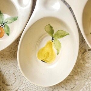 May include: Off-white ceramic serving dishes with a pear design. Each dish has a unique shape with a central bowl and a handle. The pear is yellow with green leaves, painted in a watercolor style. The dishes are likely vintage.