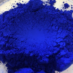 May include: Close-up of a vibrant, deep blue pigment powder. The powder is finely ground, with a textured surface and a rich, saturated color. The image highlights the intensity and depth of the blue hue, suggesting its use in art or cosmetics.