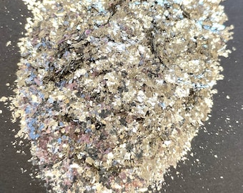 Może przedstawiać: Stos srebrnych, nieregularnych płatków. Płatki mają metaliczny połysk i odbijają światło, tworząc efekt połysku. Płatki są rozrzucone na ciemnej powierzchni.