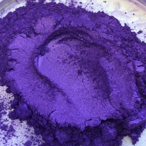 May include: Close-up of a pile of vibrant, shimmering purple pigment powder. The powder has a metallic sheen and a smooth, fine texture. The color is a deep, rich violet with hints of blue, creating a visually appealing effect. The powder is likely used for crafts or cosmetics.