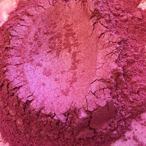Pode incluir: Close-up de um monte de p&oacute; magenta finamente mo&iacute;do e brilhante. O p&oacute; tem uma apar&ecirc;ncia texturizada e rachada, com varia&ccedil;&otilde;es de cor do bord&ocirc; escuro ao rosa brilhante. O produto parece ser um pigmento ou corante cosm&eacute;tico.