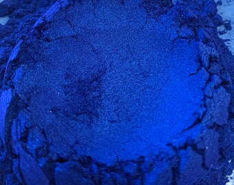 May include: Close-up of a vibrant, deep blue powder, possibly pigment or cosmetic grade. The powder has a fine texture and a slight sheen, suggesting a metallic or pearlescent quality. The color is consistent throughout the pile.
