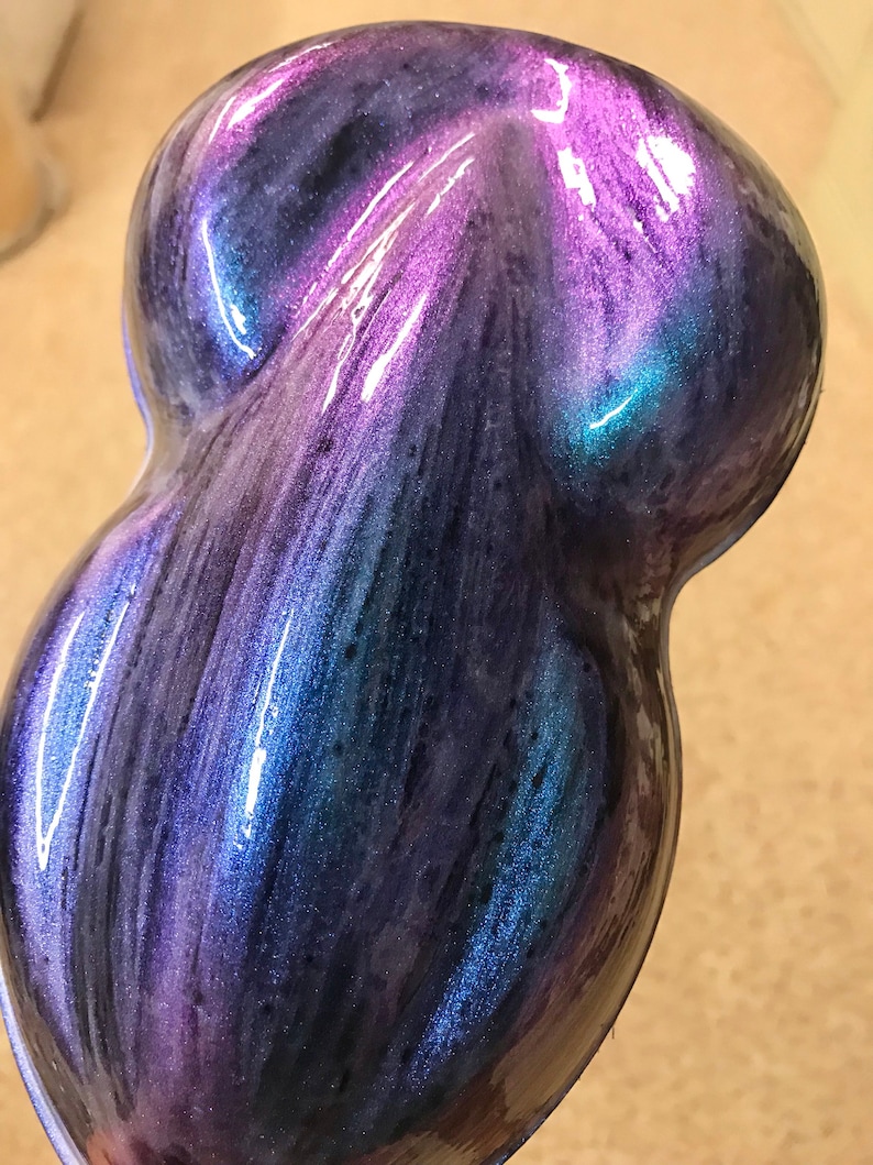 May include: A teardrop-shaped object with a glossy, iridescent finish. The colour shifts from deep blues and purples to vibrant teal and magenta, creating a dynamic effect. The surface has a smooth, flowing appearance.