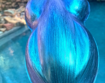 Puede incluir: Objeto en forma de lágrima con acabado metálico, que muestra una mezcla de azules y morados. La superficie tiene pinceladas visibles, creando una apariencia texturizada. El color transita del morado oscuro al azul vibrante.