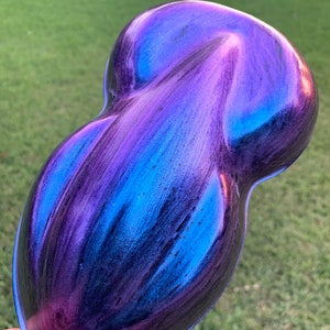 May include: A teardrop-shaped object with a vibrant, iridescent finish. The colour transitions from deep purple to shades of blue and teal, creating a dynamic, eye-catching effect. The object appears to be smooth and glossy, reflecting light.