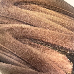 May include: Abstract art piece with a textured, swirling pattern in shades of brown and gold. The design features a blend of light and dark tones, creating a sense of depth and movement. The artwork has a grainy, almost sandy appearance.