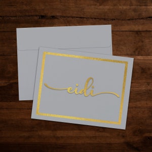 May include: A gray card with a gold border and the word "eidi" written in gold script.