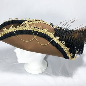 May include: A brown felt pirate hat with black and gold trim and a peacock feather accent.