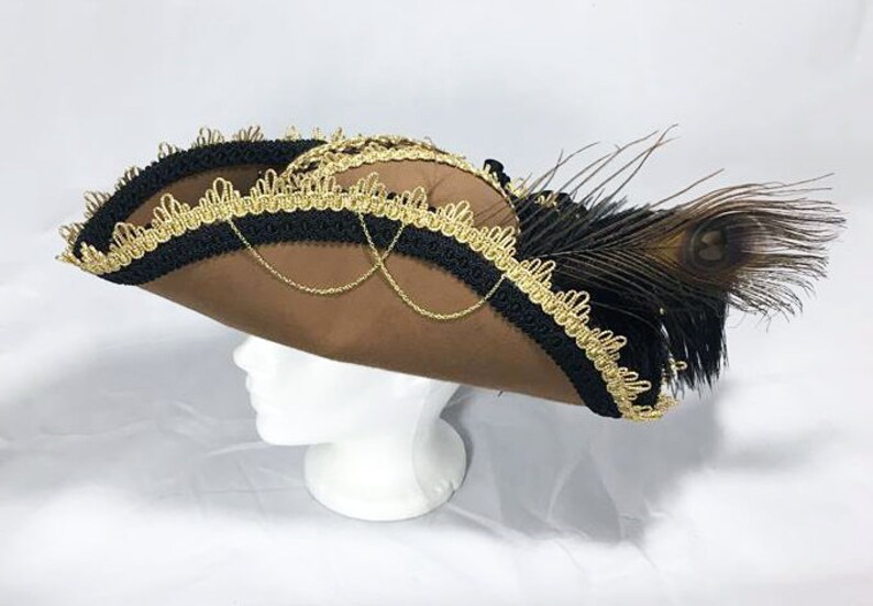 May include: A brown felt pirate hat with black and gold trim and a peacock feather accent.