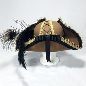 May include: A brown felt hat with a wide brim, black ribbon, and gold trim. The hat has a black feather on the side.