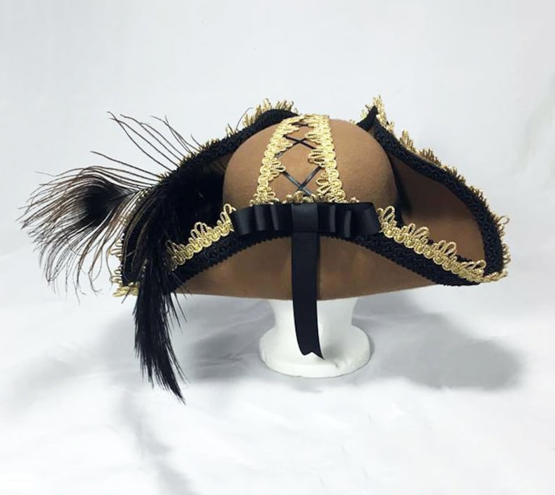 May include: A brown felt hat with a wide brim, black ribbon, and gold trim. The hat has a black feather on the side.