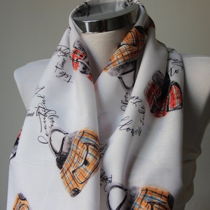 Può includere: Sciarpa di seta bianca con un motivo ripetitivo di borse a mano e il testo "Prenditi il tempo per essere consapevole, Prenditi il tempo per fiorire".