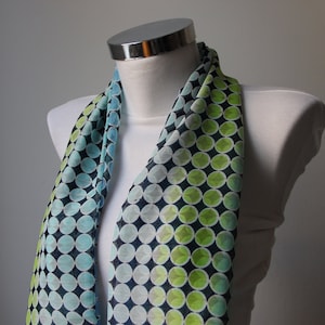 May include: A blue and green patterned scarf with a gradient of colors. The scarf is made of a sheer fabric and has a circular pattern.