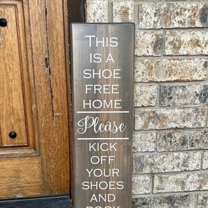 May include: A wooden sign with the text "This is a shoe free home. Please kick off your shoes and rock your socks! Thank you!" in white lettering.