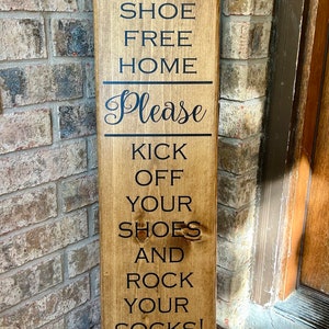 May include: A wooden sign with the text "This is a shoe free home. Please kick off your shoes and rock your socks! Thank you!"