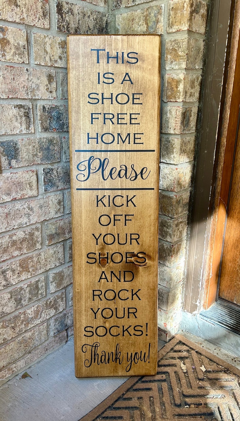 May include: A wooden sign with the text "This is a shoe free home. Please kick off your shoes and rock your socks! Thank you!"