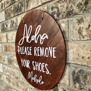 May include: A round wooden sign with the text "Aloha Please Remove Your Shoes. Mahalo" written in white paint.