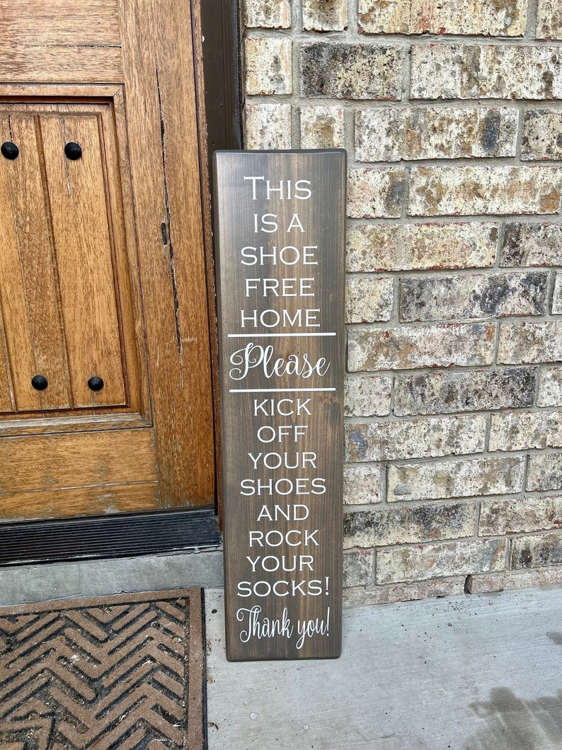 May include: A wooden sign with the text "This is a shoe free home. Please kick off your shoes and rock your socks! Thank you!"