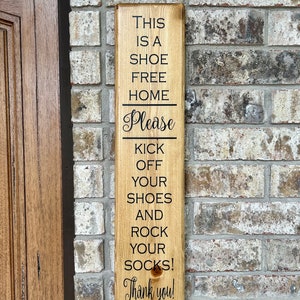 May include: A wooden sign with the text "This is a shoe free home. Please kick off your shoes and rock your socks! Thank you!"