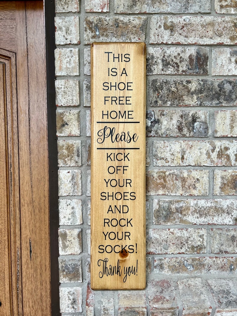 May include: A wooden sign with the text "This is a shoe free home. Please kick off your shoes and rock your socks! Thank you!"