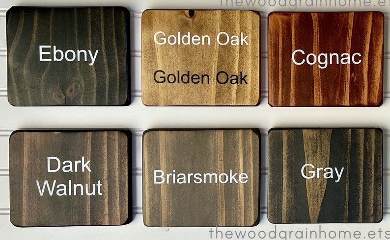 May include: Six wood stain samples in square tiles, labeled with their names: Ebony, Golden Oak, Cognac, Dark Walnut, Briarsmoke, and Gray.