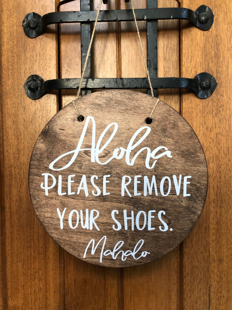 May include: A round wooden sign with the text "Aloha Please Remove Your Shoes. Mahalo" in white lettering.