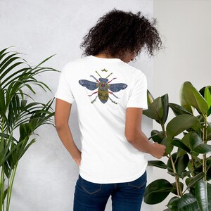May include: White t-shirt with a blue and gold bee design on the back. The bee is surrounded by swords and a crown.