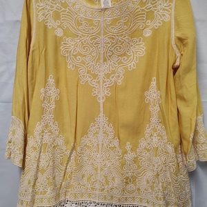 May include: Mustard yellow tunic with three-quarter sleeves and detailed white embroidery. The tunic has a round neckline and a delicate lace hem. The brand name "indigo thread co." is visible on the label.