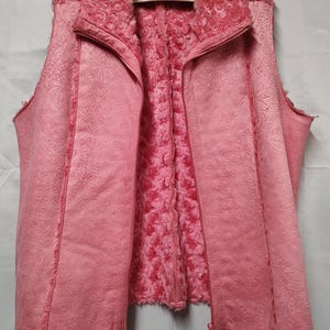 May include: A pink vest with a paisley pattern on the exterior and a plush, rose-like texture on the interior. The vest has a full zipper closure and a high collar. The vest is hanging on a white hanger.