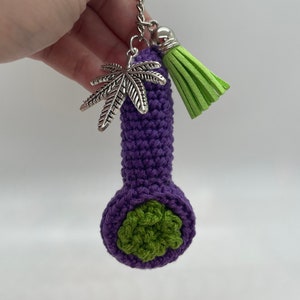 May include: Purple crocheted pipe keychain with a green leaf detail and a green tassel charm.