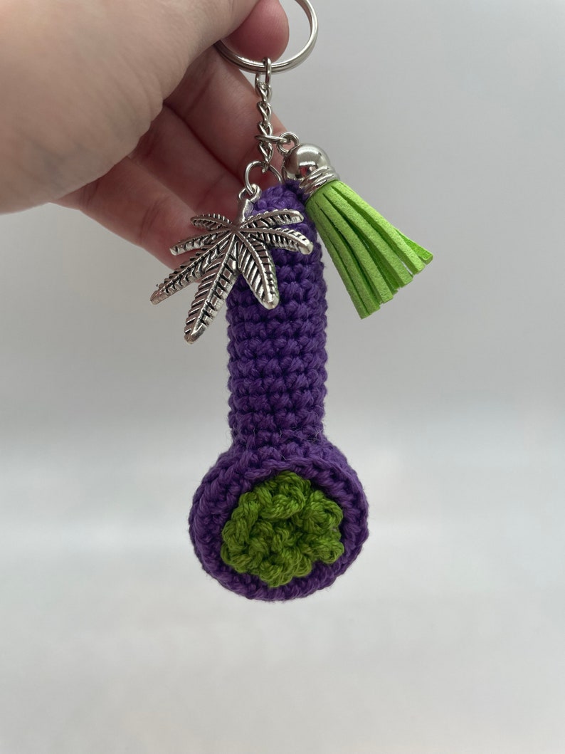 May include: Purple crocheted pipe keychain with a green leaf detail and a green tassel charm.
