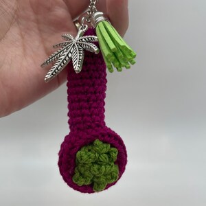 May include: A crocheted purple pipe keychain with a green marijuana leaf design and a green tassel.
