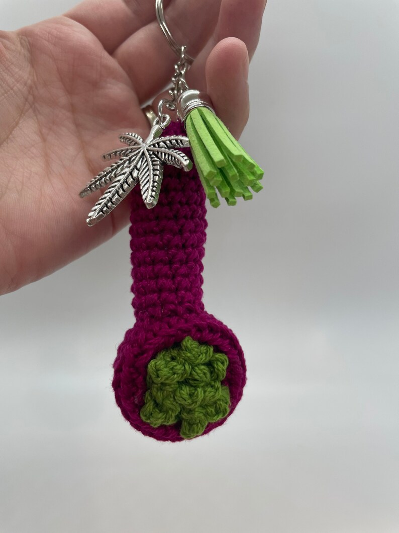 May include: A crocheted purple pipe keychain with a green marijuana leaf design and a green tassel.