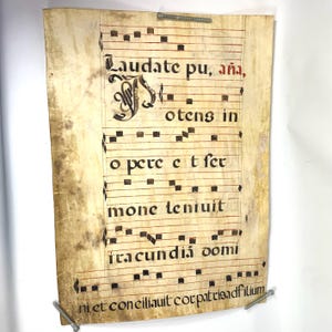 May include: Aged parchment with musical notation and Latin text. The text includes "Laudate pu, aña" and "otens in". The sheet is secured with screws. The paper has a yellowed, aged appearance.