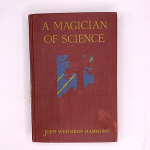 Puede incluir: Un libro antiguo titulado "A Magician of Science" de John Winthrop Hammond. La portada es de color rojo oscuro con letras doradas y un gráfico azul y amarillo. El libro muestra signos de desgaste.