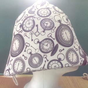 May include: A white and purple fabric hat featuring a repeating pattern of pocket watches and keys. The hat has a cone shape and a drawstring. The design is reminiscent of a vintage or steampunk aesthetic.