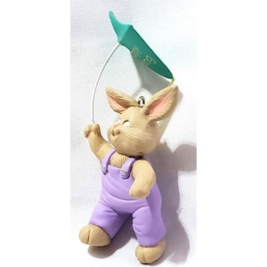 May include: A brown bunny wearing purple overalls holds a green kite with the word "Spring" written on it.