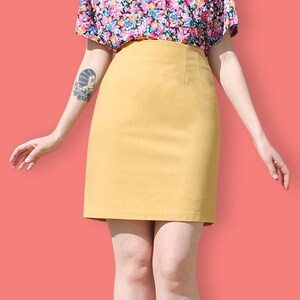 May include: A woman wearing a yellow skirt and a floral blouse. The skirt is knee-length and has a straight silhouette. The blouse is short-sleeved and has a colorful floral print.