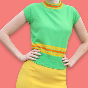 May include: A green sleeveless sweater with orange and yellow stripes at the neckline and hem. The sweater is paired with a yellow skirt.