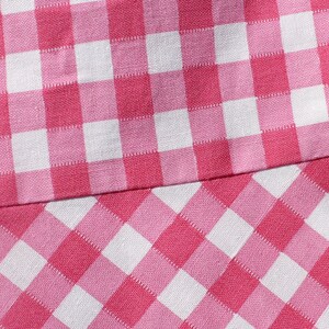 May include: Pink and white checkered fabric with a different pattern on the bottom half. The top half has a larger square pattern, while the bottom half has a smaller diamond pattern.