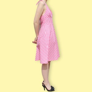 May include: A pink and white gingham dress with a halter neckline and a fitted bodice. The dress has a full skirt and is knee-length.