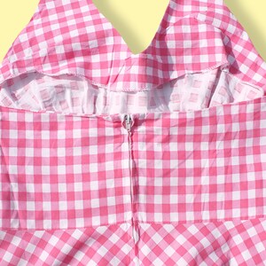 May include: Back view of a pink and white gingham dress with a zipper closure.