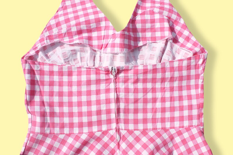 May include: Back view of a pink and white gingham dress with a zipper closure.