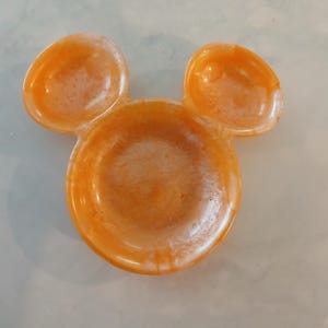 May include: Orange resin dish shaped like a mouse head, with two ear-shaped dishes above the main bowl. The dish has a glossy finish and a marbled effect.