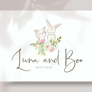 May include: A white cat and a white rabbit with pink noses are sitting in a bouquet of pink, white, and blue flowers. The text "Luna and Boo Boutique" is written in brown cursive script below the animals.